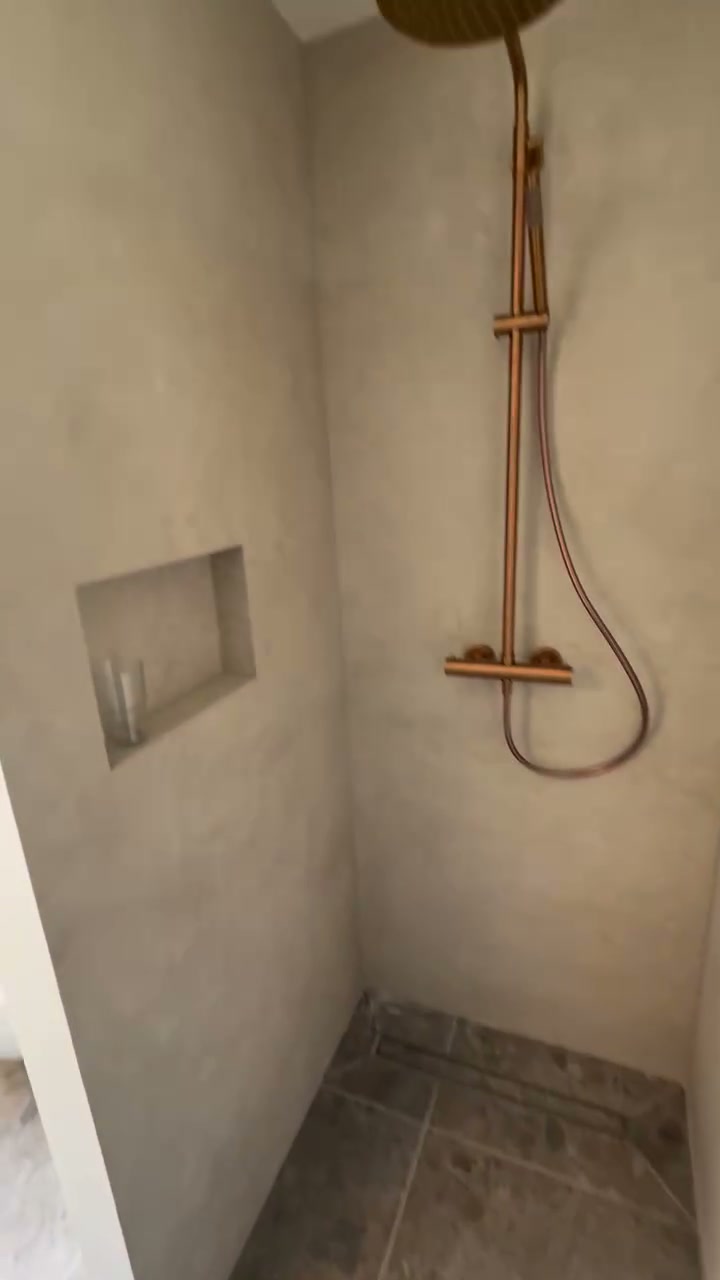 Koperen regendouche en handdouche op een wand met betonlook tegels en een nis