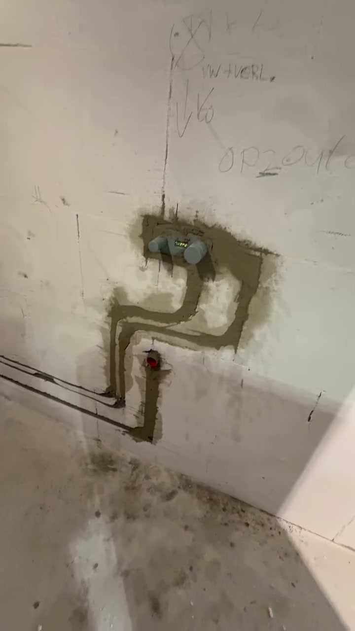 Kale badkamerwand met nieuw ingefreesde leidingen en een douchekraanaansluiting, klaar om te tegelen