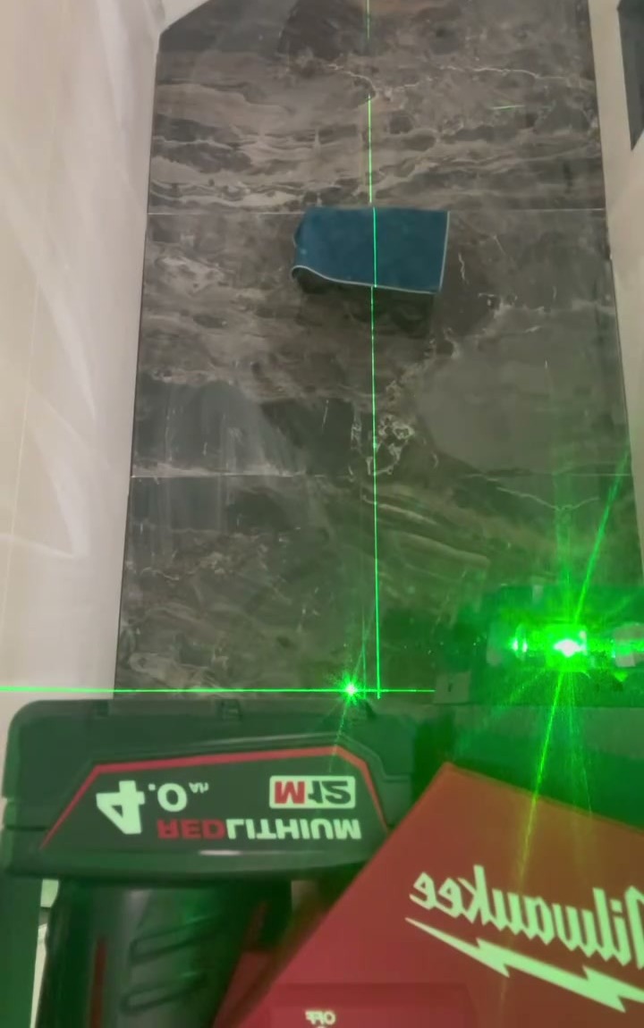 Wand met donkere marmerlook tegels die met een groene laserlijn waterpas worden gezet